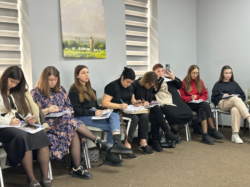 Participants sit in a row with notebooks during a training session.